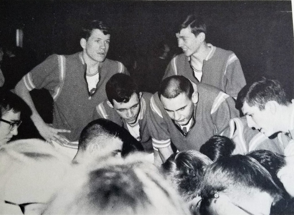 From 1966 Yearbook, Sophomore year.  
L-R, players in our class: Steve Hoane (standing), Dave Zellers (crouching), and Bob Yeager (standing). Concentrating on the coachs instructions during a time out.